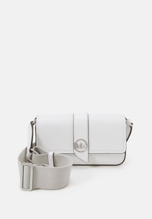 Sac bandoulière blanc Michael Kors avec fermeture à rabat et logo MK argenté, avec une large sangle réglable en tissu beige sur fond blanc.