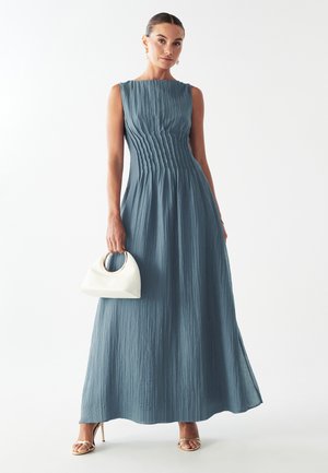 Maxi šaty z textúrovaného, tlmeného modrého materiálu s detailmi plisovania, bez rukávov, doplnené bielou kabelkou s obľúbeným okrúhlym uchom.
