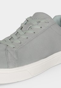 Baskets en daim gris clair avec des lacets assortis et une semelle en caoutchouc blanche vues de côté.