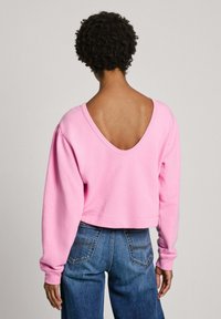 Rozā kropta sporta krekls ar dziļu V veida aizmuguri, garām piedurknēm un ribotiem aprocēm, apvienots ar augsto vidukli ziliem džinsiem.