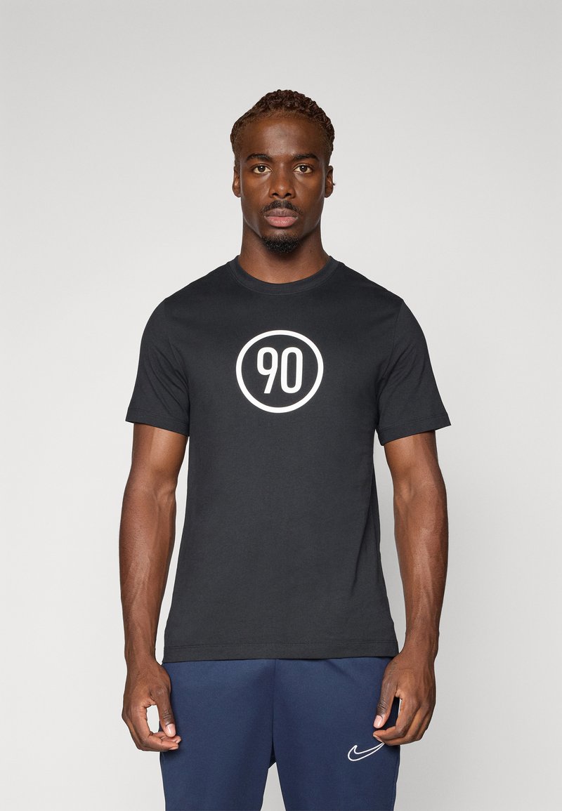 T-shirt en coton noir avec un graphique rond blanc affichant "90". Manches courtes et design col rond, associé à un short bleu marine.
