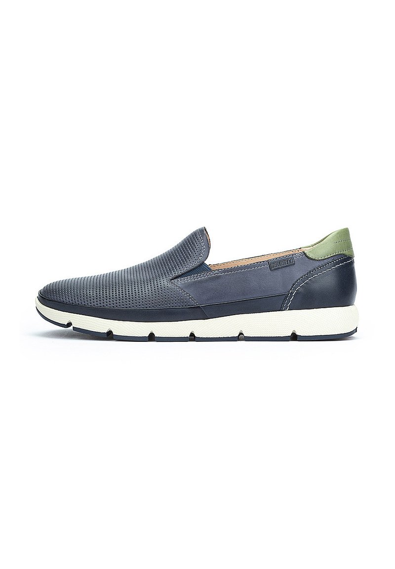 Zapato deslizante navy con parte superior perforada, acento verde en el talón y suela de goma blanca, que presenta un diseño elegante y aerodinámico.
