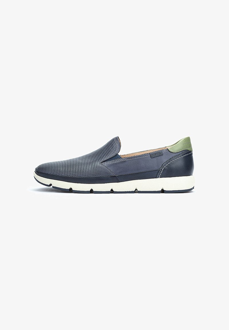 Zapato deslizante navy con parte superior perforada, acento verde en el talón y suela de goma blanca, que presenta un diseño elegante y aerodinámico.