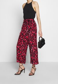 Rote und schwarze Leopardenmuster-Hosen mit weitem Bein, hohem Bund und Schleifendetail, kombiniert mit einem schwarzen Neckholder-Top und Riemchen-Heels.