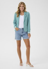 Blazer bleu pâle avec des poignets rayés blancs, associé à un short en denim. Le blazer a un col cranté et une fermeture à un bouton.