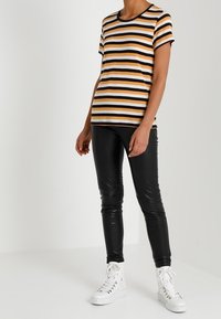 Pruhované tričko v oranžové, bílé a černé barvě, kombinované s lesklými černými legínami a bílými vyššími teniskami. Casual střih s krátkým rukávem.