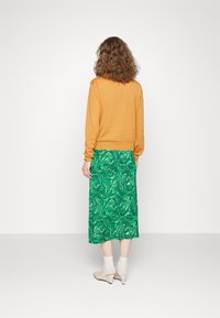 Pomarańczowy sweter, zielona spódnica w marmurkowy wzór, o długości midi, gładka tekstura, połączona z jasnobeżowymi obcasami i białymi skarpetkami do kostek.