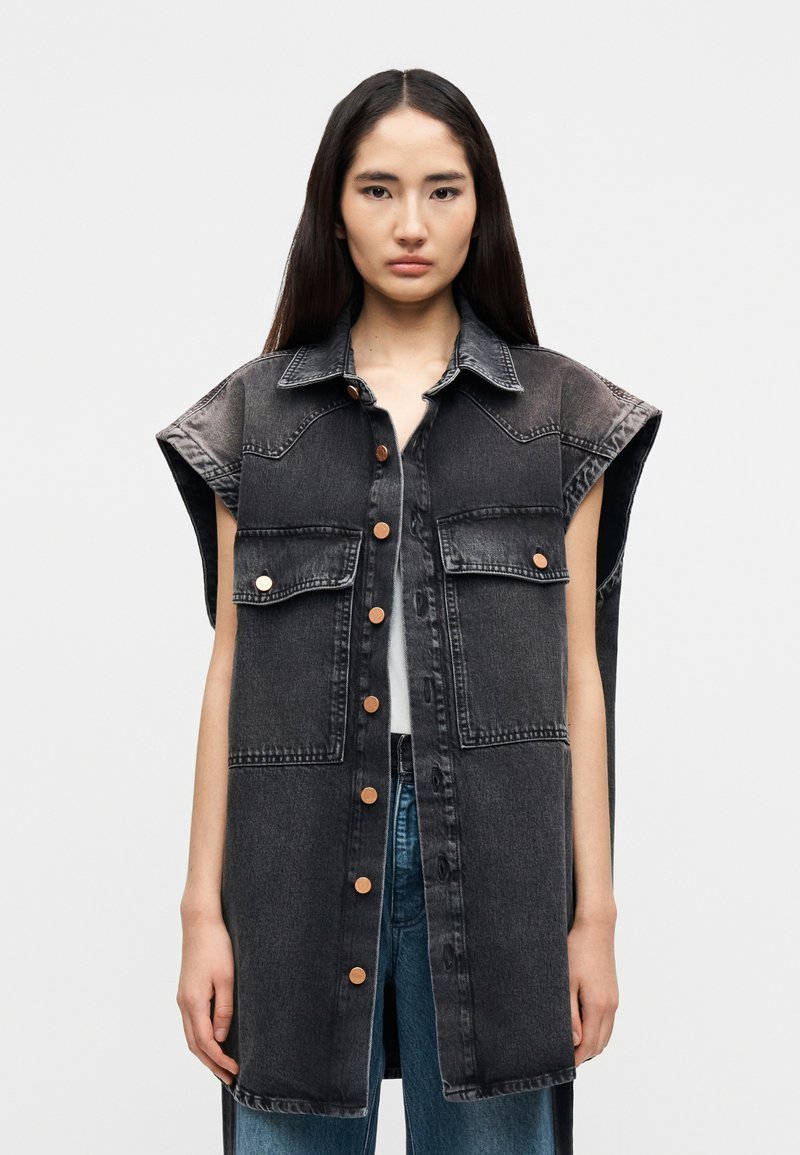 Μαύρο αμάνικο πουκάμισο από τζιν με δύο μπροστινές τσέπες, καφέ κουμπιά και γιακά. Διαθέτει φαρδιά, oversized εφαρμογή και ίσιο τελείωμα.