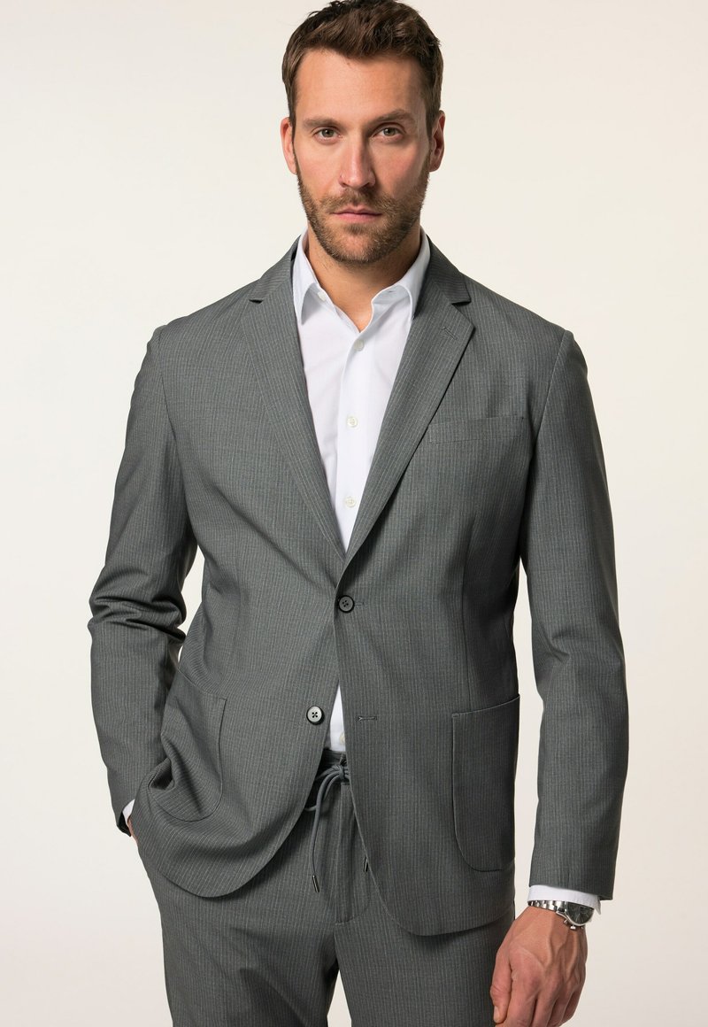 Completo grigio a righe con giacca monopetto, due tasche frontali e pantaloni con coulisse, abbinato a una camicia bianca a maniche lunghe.