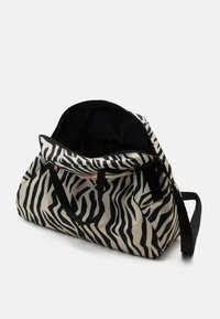 Gran bolsa de viaje a rayas de cebra en crema y negro, con resistentes asas negras y una parte superior abierta que revela un amplio interior forrado en negro.