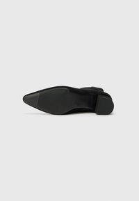 Bottine noire en daim à talons, avec un bout pointu et une semelle en caoutchouc texturée. Présente un design épuré et une finition lisse.