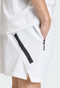 Λευκά σορτς από ελαφρύ ύφασμα με μαύρη τσέπη με φερμουάρ και μαύρη ρίγα, με άνετη εφαρμογή και πλευρικές σχισμές.