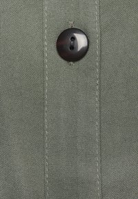 Hemd aus grauem Stoff mit schwarzen Knöpfen, sichtbaren Nähten und einer strukturierten Oberfläche. Einfaches Design ohne Muster.