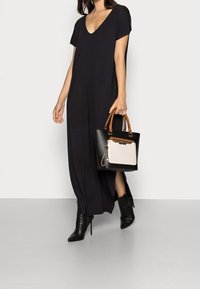 Svart maxiklänning med korta ärmar och djup V-ringning, tillsammans med en svart handväska med en krämfärgad framficka och bruna handtag. Svarta högklackade stövlar.