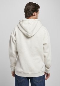 Felpa grigia chiaro in pile con finitura testurizzata, grande cappuccio e orlo e polsini a coste. Indossata con jeans in denim scuri.