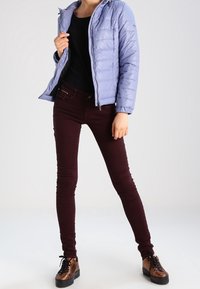 Ljuslila puffjacka, svart topp, vinröda skinny jeans och bruna snörskor med tjock sula, vilket visar en avslappnad outfit.