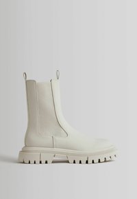 White ankle boots with a smooth leather finish, elastic side panels, and a chunky textured sole with deep grooves. Minimalistic design.