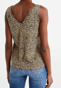 Halenka bez rukávů s leopardím vzorem v béžové a černé barvě, s hlubokým vykrojením na zádech. Tkanina se zdá být hladká a má volný střih.
