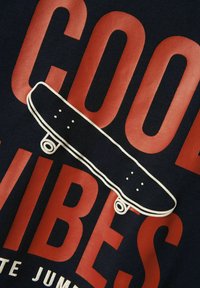 Tejido azul marino con un texto rojo audaz que dice "BUENAS VIBRAS" y un gráfico de patineta en contorno blanco en el centro.