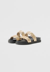 Sandalene med gullvevde stropper og svart gummisåle. Har to krysset stropper og et flatt design.