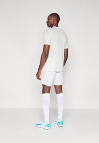 Light gray athletic t-shirt paired with white shorts, white socks, and blue soccer cleats. Features a smooth texture and fitted design.