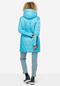 Blue quilted puffer jacket with a hood, featuring a textured pattern, long sleeves, and zippers at the cuffs. Paired with light blue jeans.