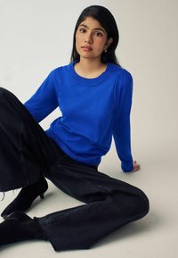 Pull bleu à manches longues avec un col côtelé, associé à un jean noir à jambes larges et des bottines noires. Texture douce, coupe décontractée.