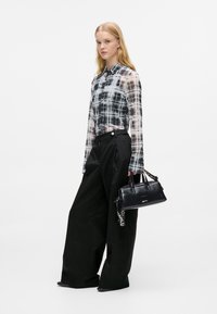 Transparente schwarz-weiße karierte Bluse mit langen Ärmeln, kombiniert mit weiten schwarzen Hosen und einer kleinen schwarzen Handtasche.