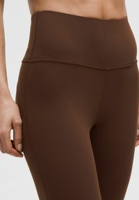 Braune hochtaillierte Leggings mit einer glatten Textur, elastischem Bund und Nahtdetails an den Seiten für einen figurschmeichelnden Look.