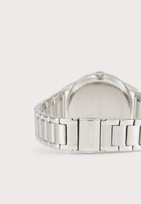 Reloj de acero inoxidable plateado con un acabado pulido, que cuenta con un diseño de pulsera eslabonada, caja redondeada y logotipo grabado en el cierre.
