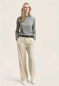 Sweter z golfem w jasnoszarym kolorze, kremowe plisowane spodnie, czarny pasek i białe trampki. Gładka faktura, luźny fason i swobodny styl.