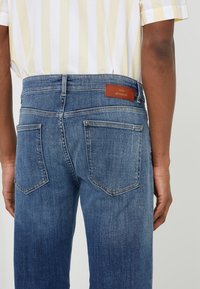 Miesten siniset farkut ovat suoralinjaiset, viidellä taskulla, takana vyötäröllä on nahkainen bränditunnus ja niissä on kevyt haalistuminen.