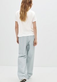 T-shirt blanc léger à manches courtes associé à un pantalon large rayé bleu clair, avec des poches arrière et une coupe décontractée.