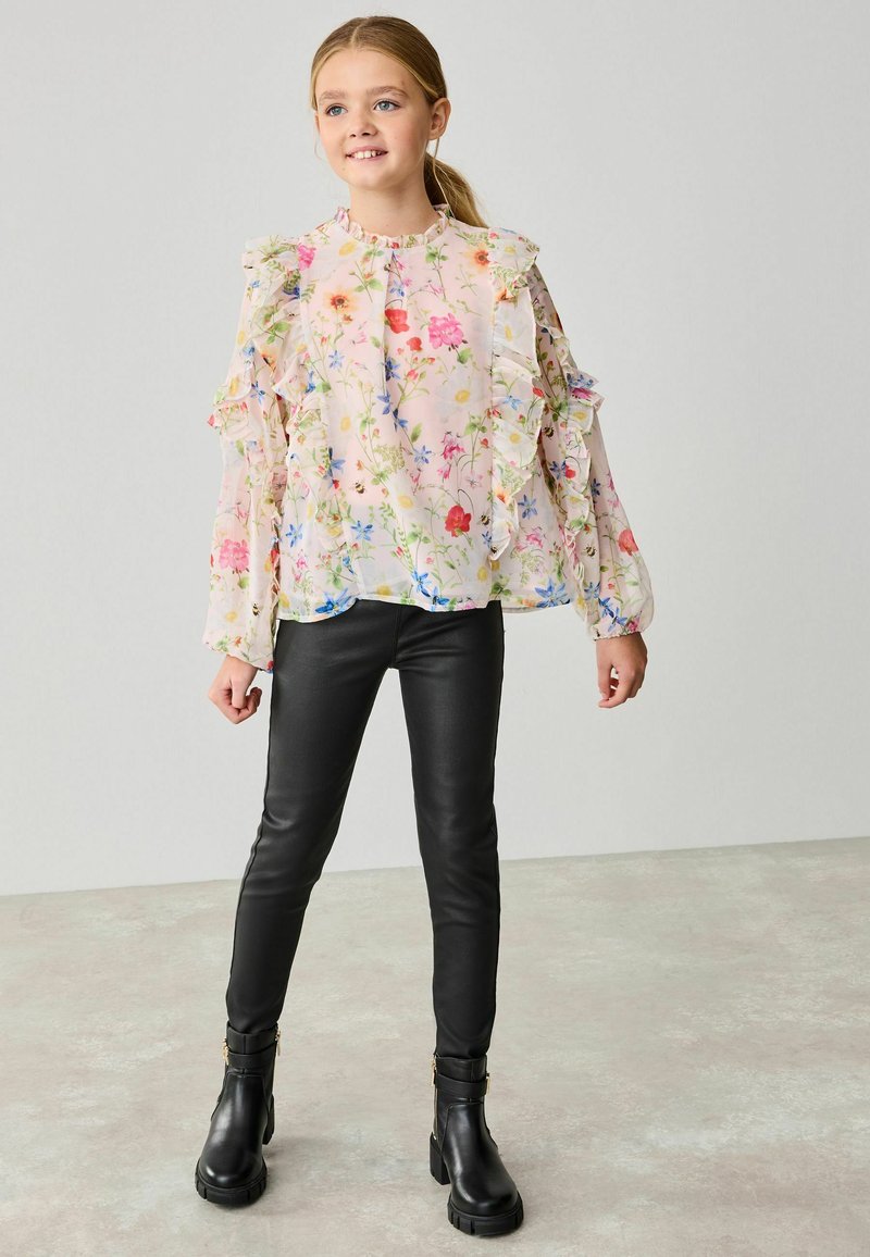 Blommig blus med volanger, med en ljusrosa bakgrund och färgglada blommönster; kombinerad med svarta tajta byxor och ankelboots.