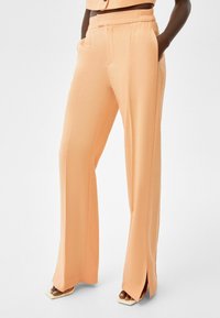 Peach wide-leg trousers with a smooth texture, featuring side pockets and split hems, made of lightweight fabric for comfort.