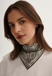 Czarnobiały szalik w wzór paisley w kształcie trójkąta z zagiętym kołnierzem. Gładka faktura tkaniny i kontrastowe detale brzegowe.