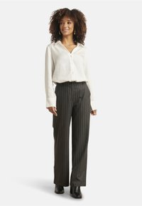 White button-up shirt and black pinstriped trousers. Smooth fabric, relaxed fit, long sleeves, and ankle-length cut. Black heeled boots.