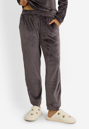 Pantalones de pijama de terciopelo gris carbón con cintura elástica, decorados con pequeños patrones de estrellas. Llevados con zapatillas color crema adornadas con formas de corazones.