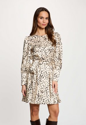 Mujer con vestido de manga larga, estampado de leopardo beige y cinturón en la cintura, de pie contra un fondo claro y liso.