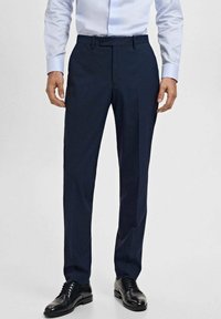 Pantalon de costume bleu marine en tissu lisse, présentant une coupe droite, des passants de ceinture et des poches latérales inclinées, associé à des chaussures de ville noires.