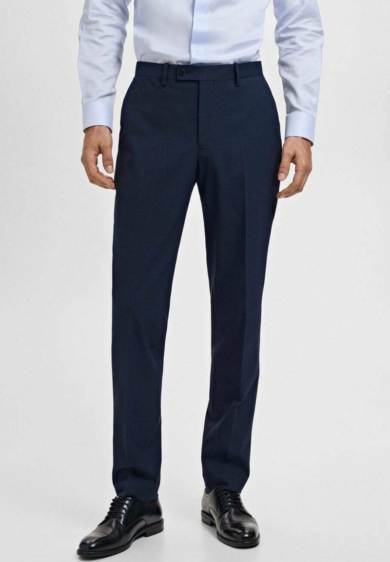 Pantalon de costume bleu marine en tissu lisse, présentant une coupe droite, des passants de ceinture et des poches latérales inclinées, associé à des chaussures de ville noires.