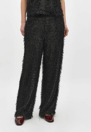 Zwart fuzzy twee-delig outfit met een textuurtop en wijdvallende broek. Opvallende glanzende rode schoenen met decoratieve accenten.