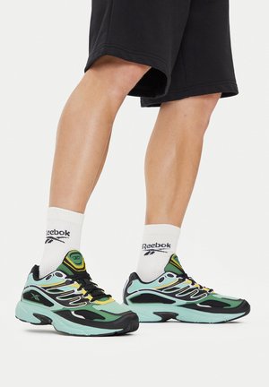 Czarno-turkusowe trampki z żółtymi akcentami. Cholewka z siateczki i gumowa podeszwa. W połączeniu z białymi skarpetkami z logo, noszone z czarnymi szortami.