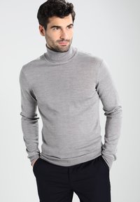Grå ribbestrikket genser laget av mykt stoff, med lange ermer og en tettsittende silhuett. Kombinert med marineblå bukser.