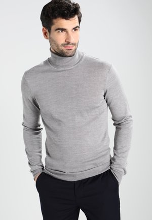 Pull col roulé gris en tricot doux, avec des manches longues et une silhouette ajustée. Associé à un pantalon bleu marine.