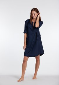 Abito blu marina con vestibilità comoda, scollatura a V, maniche arrotolate e tasche laterali. Realizzato in un tessuto morbido con una silhouette alla lunghezza del ginocchio.