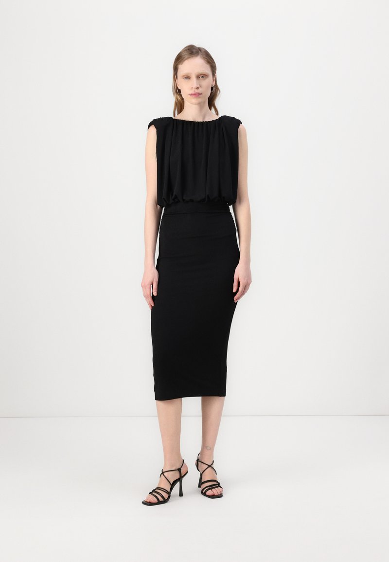 Black sleeveless dress with gathered bodice and fitted midi skirt. Smooth fabric texture. Styled with black strappy high heel sandals.