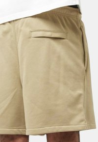 Pantaloni shorts in cotone beige con vita elastica, tasca piatta sul retro e dettaglio sui lati con texture liscia.