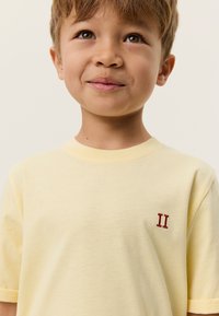 Κοντομάνικο κίτρινο βαμβακερό μπλουζάκι με μικρή κόκκινη κεντητή «II» στη αριστερή πλευρά του στήθους. Λείο ύφασμα και άνετη εφαρμογή.