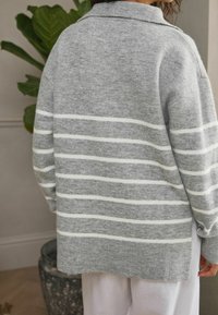 Pull en tricot gris avec des rayures horizontales blanches, doté d'un col et d'une coupe décontractée. Texture douce et manches longues.
